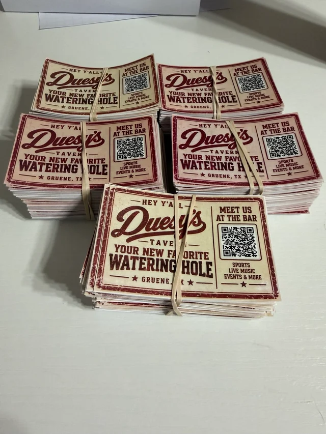 Stacks of Duesy's Tavern promotional stickers reading Your New Favorite Watering Hole and Meet Us at the Bar, with QR codes