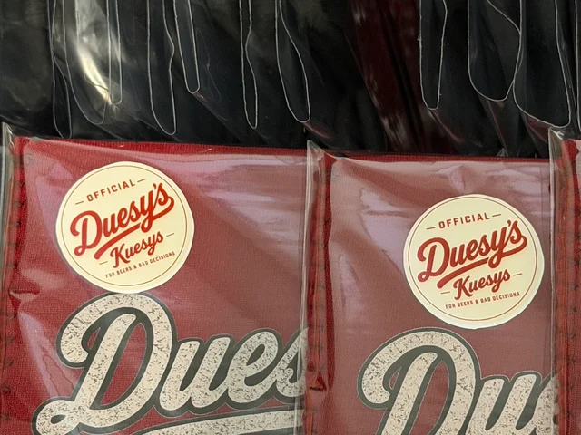 Close-up of Official Duesy's Kuesy's stickers on packaged red koozies